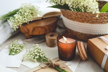 Festive concept, lily of the valley bouquet, gift box , burning candle and letter
