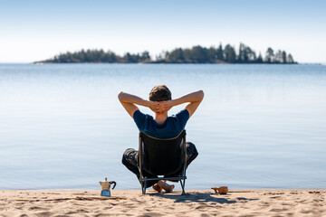 A man is resting in a camping chair on the seashore.