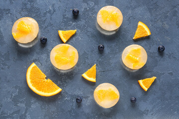 Fototapeta na wymiar Fresh blueberry, orange and pieces frozen in ice on blue background