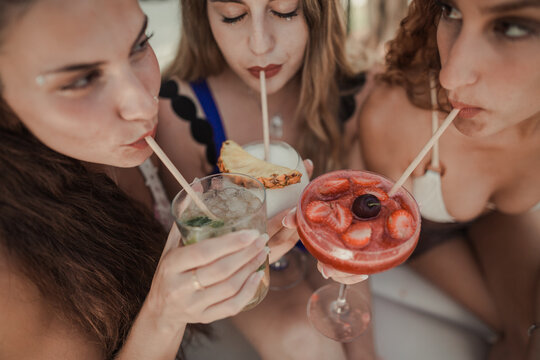 Women sucking straws from cocktails together outdoors