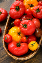 Wicker bowl with different fresh tomatoes on wooden background