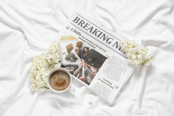 Beautiful lilac flowers with newspaper and cup of coffee on bed