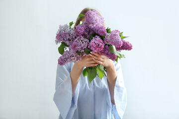Young woman holding bouquet of beautiful lilac flowers near white wall - obrazy, fototapety, plakaty