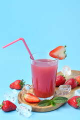 Fototapeta Board with glass of tasty strawberry juice and ice cubes on blue background obraz