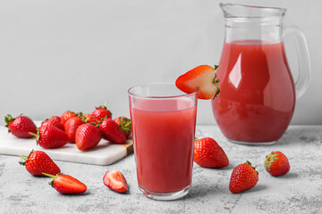 Glass and jug of tasty strawberry juice on grey table