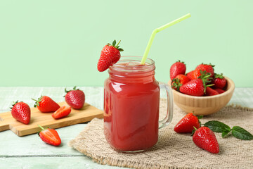 Mason jar of juice and bowl with strawberry on green wooden table