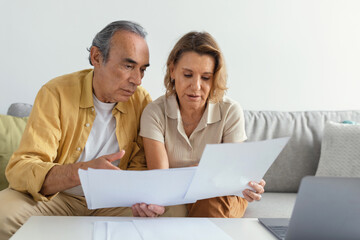 Budget planning concept. Senior spouses looking at papers and calculating family spends together
