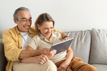 Retirement and internet fun concept. Excited senior spouses using digital tablet, websurfing or watching film online