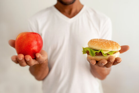 Black Man Holding Burger And Apple Against White Background, Cropped