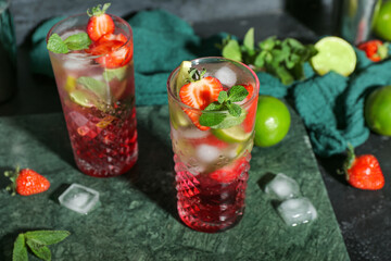 Glasses of delicious strawberry mojito on dark background, closeup