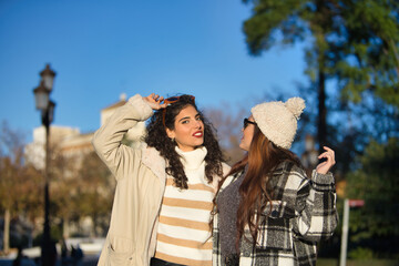 Fototapeta premium Two women, young and beautiful, with sweater, sunglasses, coat and one with wool hat, embraced, looking at each other, very smiling and happy. Concept autumn, winter, cold, friendship, full happiness.