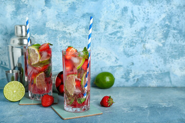 Glasses of fresh strawberry mojito with jigger and shakers on grunge blue background