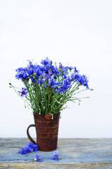 Bouquet of blue cornflowers in a clay mug on an old wooden board, soft selective focus. Floral background with wildflowers