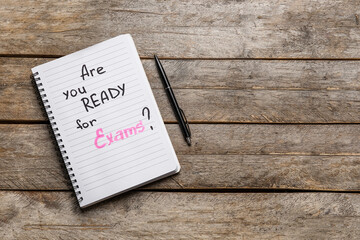 Notebook with question ARE YOU READY FOR EXAM? and pen on brown wooden background