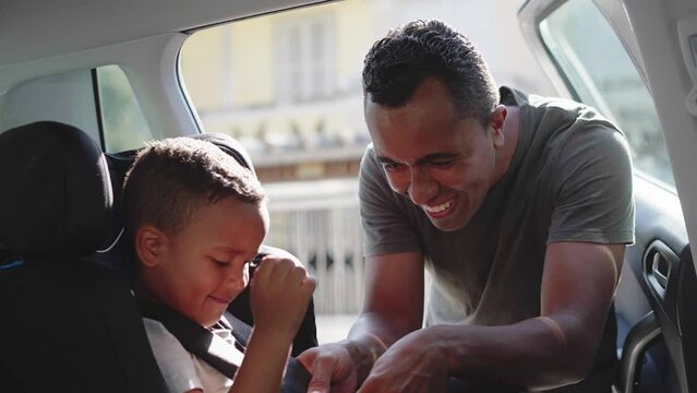 safe ride, loving father puts his little cute male child in back seat in baby car seat and fasten safety belts before driving
