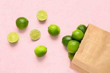 Paper bag with fresh limes on pink background