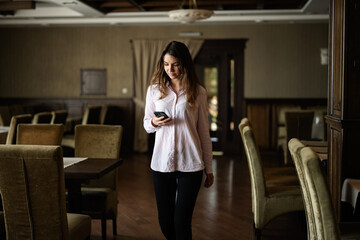 Young beautiful brunette woman walk in restaurant and look at phone.