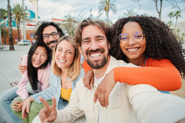 Group of multiracial friends smiling and taking a selfie portrait. Young people having fun on a social gathering. Joyful team of happy youngsters shooting a self foto with a cellphone on a meeting