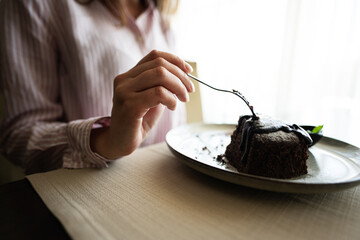 Close up hand woman sit in coffee shop cafe restaurant indoors and eat chocolate brownie dessert cake.