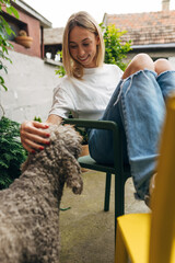 A beautiful blond woman pats a dog in the garden.