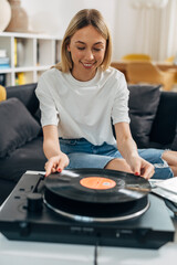 A pretty blond woman plays vinyl records at home.