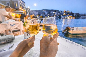 Raising hands holding a glass of white wine in front of a seaside village at a greek restaurant.