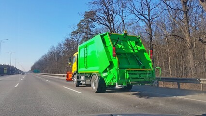 A new green garbage collection vehicle is moving along the highway. Transportation of human waste products. Disposal of municipal waste. Ecological infrastructure of the metropolis