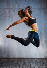 Young slim sports woman in black clothing jumping on gray wall background