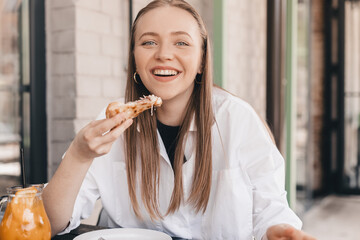 Woman eating tasty pizza outdoor in street cafe. Fast food takeaway in sunny day. Blonde woman wear white shirt, orange lemonade and pizza on restaurant table. Female enjoy of delicious slice pizza.
