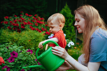 Young woman and her one year child care flowers in the garden