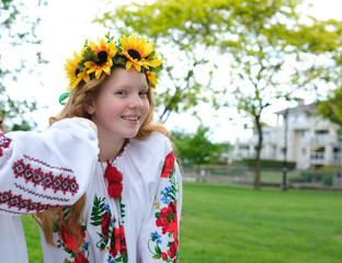 sunny girl with bright red hair stands against background of green trees with wreath of sunflowers embroidered national shirt Ukrainian woman for peace No war Victory of Ukraine national patriotism