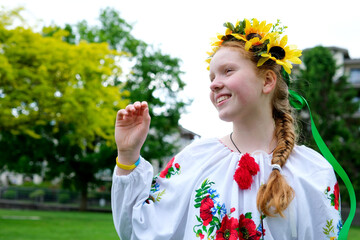 sunny girl with bright red hair stands against background of green trees with wreath of sunflowers embroidered national shirt Ukrainian woman for peace No war Victory of Ukraine national patriotism
