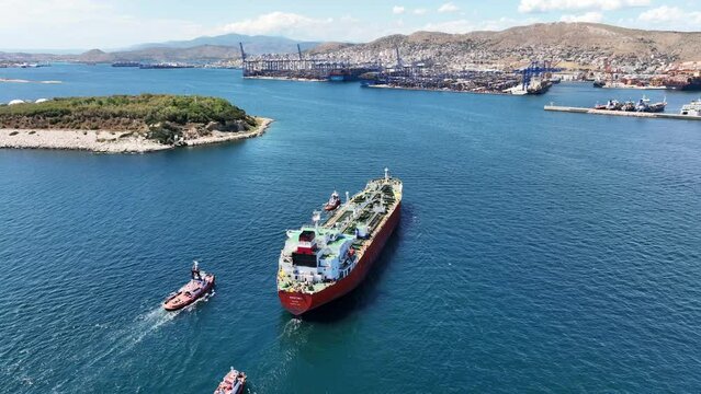 Aerial drone video of huge crude oil tanker assisted by tug boats cruising near container terminal of Perama, Piraeus, Attica, Greece