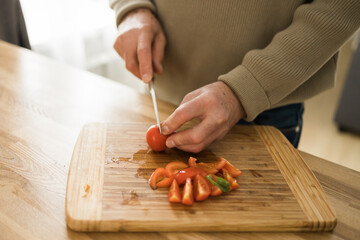 Unrecognizable senior man cutting tomatoes on a chopping board at kitchen