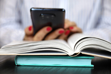 Woman reading a book while sitting at table with smartphone in hands. Concept of education and literature