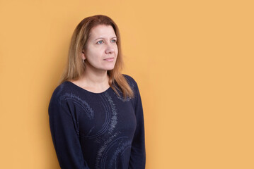Obraz premium On a yellow background, a middle-aged woman in dark blue sweater looks forward and up with hope and love, the woman has a strong faith that everything will be fine in the future, she prays