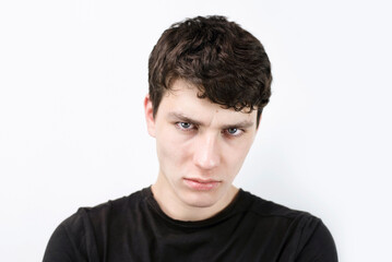 Fototapeta premium A guy of 18 years old with emotions of sadness and disappointment on a light background, after stress during study and work, the boy suffers from depression and headache, the boy has red eyes