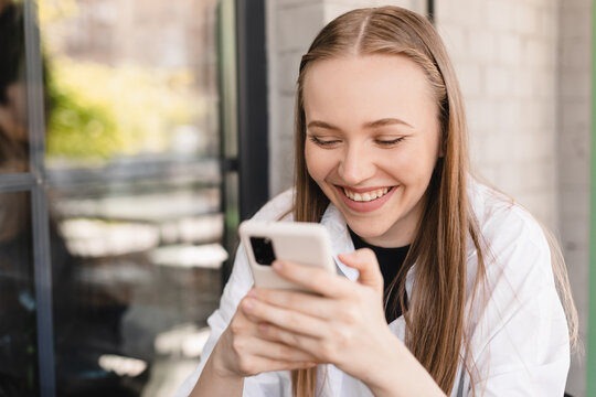 Blonde happy woman smiling reading good news on mobile phone during rest in coffee shop, happy caucasian female watching her photos on cell telephone while relaxing in cafe during free time, banking.