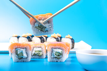Sushi rolls, with cheese and salmon, cheese, daikon and spicy sauce, with a bowl of soy sauce on a blue background
