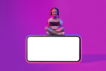 Happy kid sitting on phone with mockup, using tablet, headphones