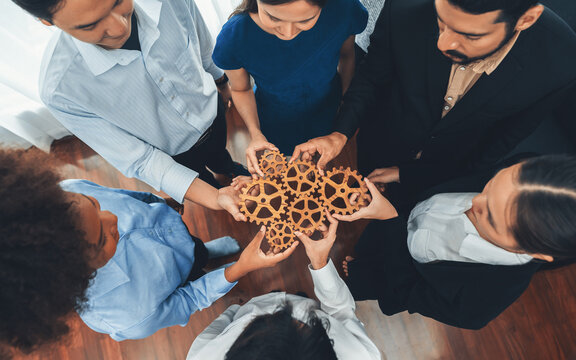 Office worker holding cog wheel as unity and teamwork in corporate workplace concept. Diverse colleague business people showing symbol of visionary system and mechanism for business success. Concord