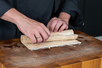 Close up of sushi chef hands preparing japanese food. Man cooking sushi with red caviar, avocado and cheese at restaurant. Traditional asian seafood rolls on cutting board.