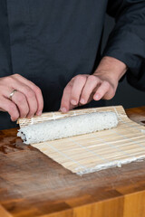 Close up of sushi chef hands preparing japanese food. Man cooking sushi with red caviar, avocado and cheese at restaurant. Traditional asian seafood rolls on cutting board.