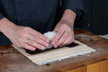 Close up of sushi chef hands preparing japanese food. Man cooking and making rice for sushi at restaurant. Traditional asian seafood rolls on cutting board.