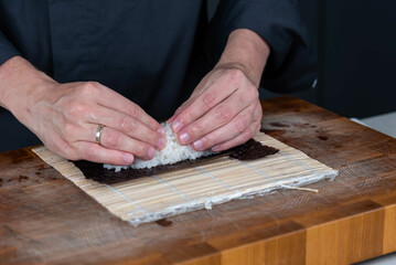 Close up of sushi chef hands preparing japanese food. Man cooking and making rice for sushi at restaurant. Traditional asian seafood rolls on cutting board.
