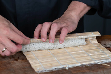Close up of sushi chef hands preparing japanese food. Man cooking sushi with red caviar, avocado and cheese at restaurant. Traditional asian seafood rolls on cutting board.