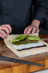Close up of sushi chef hands preparing japanese food. Man cooking sushi at restaurant. Traditional asian seafood rolls on cutting board.