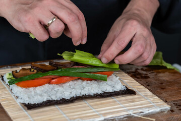 Close up of sushi chef hands preparing japanese food. Man cooking sushi at restaurant. Traditional asian seafood rolls on cutting board.