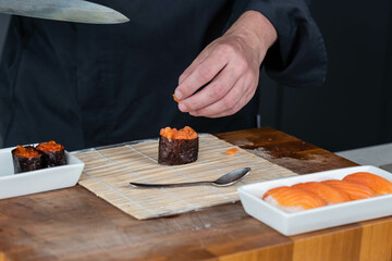 Close up of sushi chef hands preparing japanese food. Man cooking sushi with red caviar and salmon at restaurant. Traditional asian seafood rolls on cutting board.