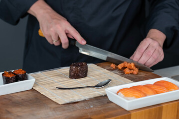 Close up of sushi chef hands preparing japanese food. Man cooking sushi with red caviar and salmon at restaurant. Traditional asian seafood rolls on cutting board.